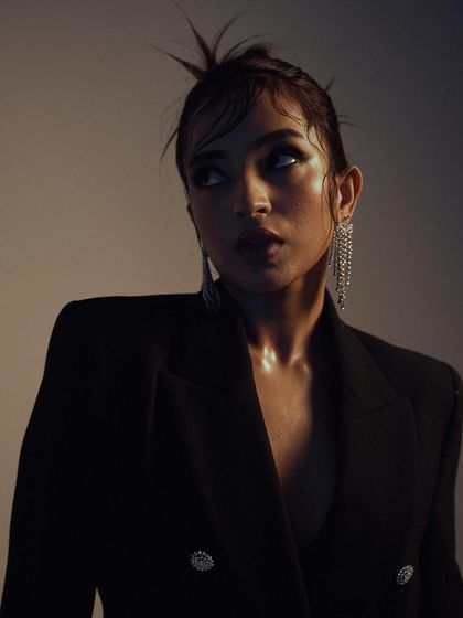 A dramatic, low-key portrait with a focus on light and shadow. The lighting sculpts the model's face and highlights the glittering earrings, creating a moody and high-fashion image.