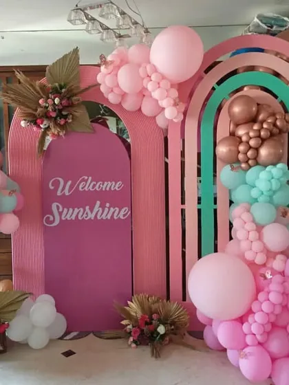 Welcoming a little sunshine with this bright and cheerful setup. The pink rainbow-themed backdrop is decorated with pastel balloons and floral accents.