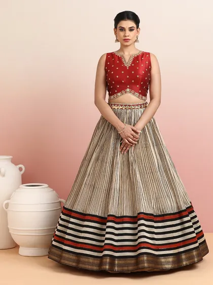 A contemporary striped silk lehenga in beige, black, and red, paired with a deep red embroidered blouse. This is a modern take on festive wear.
