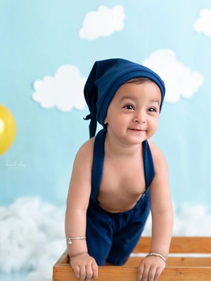 A smiling baby boy peeks out of a wooden crate in a playful moment from his sitter session.