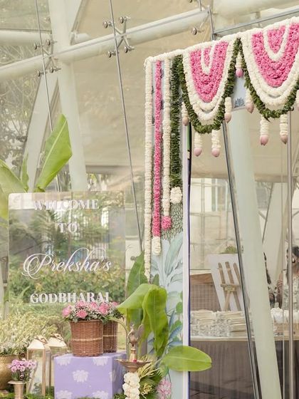 The entrance decor for the lotus-themed Godh Bharai, featuring a custom welcome sign, lush greenery, and baskets of fresh pink lotuses and roses.