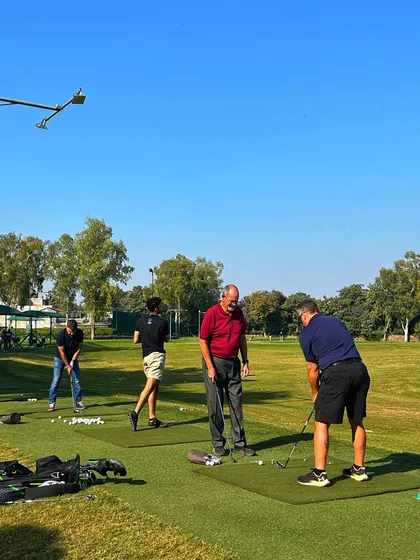 A coach gives a lesson to a player on the grass tee, demonstrating our commitment to helping you improve.