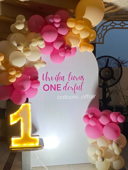 A close-up of the 'Urvika turns Onederful' backdrop with its pink and peach balloon garland.