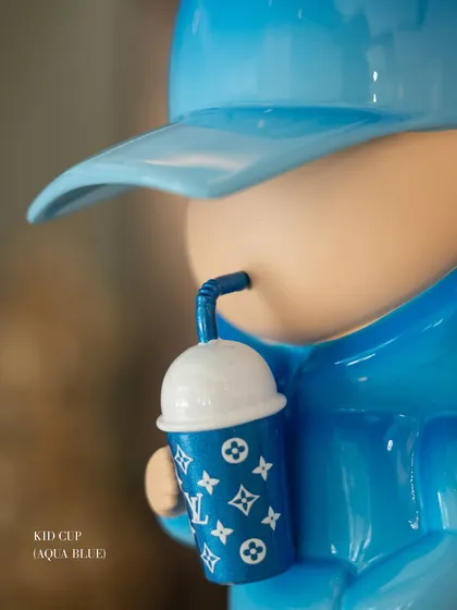 A detail shot of the aqua blue "Kid Cup" sculpture, focusing on the monogrammed cup it holds.
