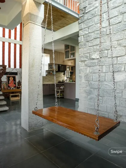The indoor swing is a favorite feature in many homes I design. Here, it is suspended between a concrete pillar and a rugged stone wall, creating a perfect spot to relax and enjoy the view of the open-plan interior and puja area.