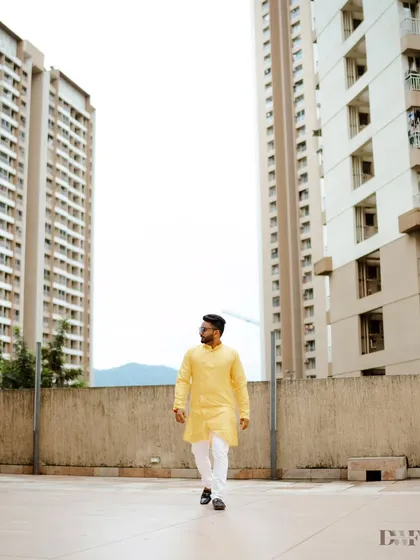 A stylish shot of the groom walking in his Haldi outfit, with modern buildings in the background creating a cool urban contrast.