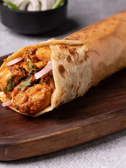 A delicious chicken tikka roll on a wooden board, styled by a professional chef. We often collaborate with chefs to ensure the food styling is authentic and appetizing.