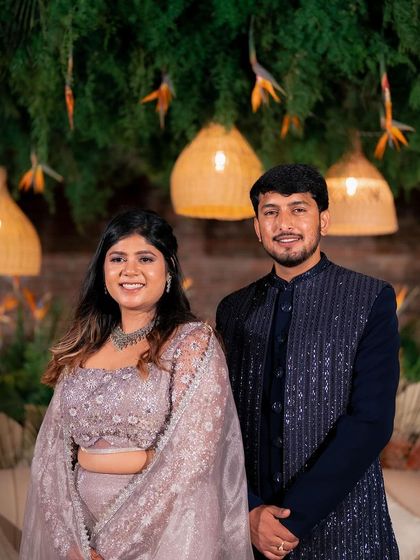 A formal portrait of the couple, looking poised and happy. The rich textures of the backdrop, from the brick wall to the pampas grass, add depth and interest to the photo.