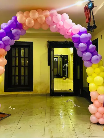 A colorful balloon archway to welcome guests to a birthday celebration, using a bright palette of purple, pink, orange, and yellow.