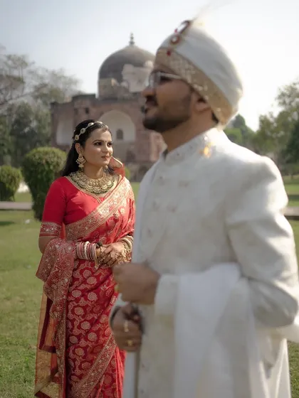 A beautifully composed shot with the bride in sharp focus, looking towards her groom who is softly blurred in the foreground, set against a historic monument.