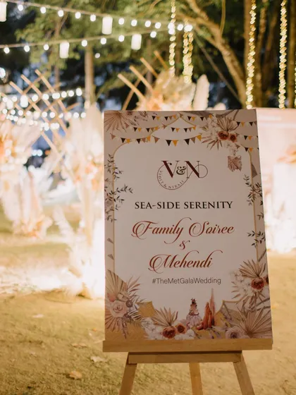 The welcome sign for the "Family Soiree & Mehendi," featuring custom graphics that reflect the boho, seaside theme of the event.