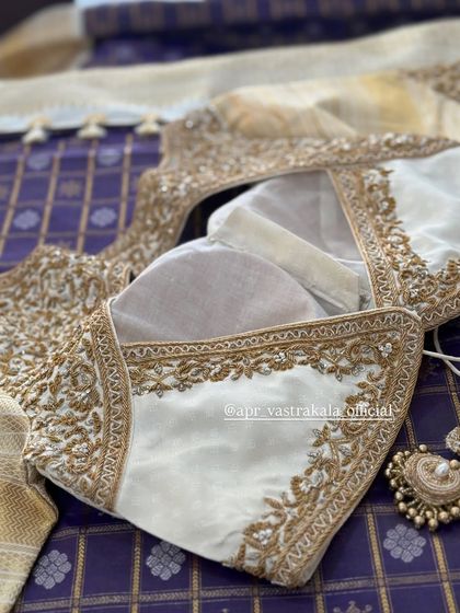 A white blouse with a sheer back panel and gold floral embroidery.