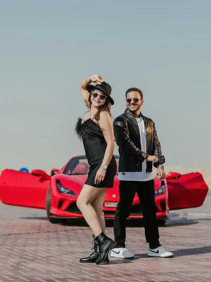 A cool, edgy pre-wedding shot in the Dubai desert featuring a vibrant red Ferrari. The couple's leather jackets and confident poses create a powerful, movie-poster look.