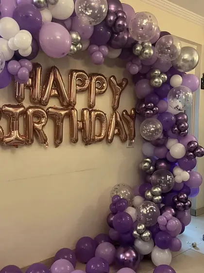 A balloon garland on the wall is a great way to decorate a smaller space. This one uses purple, white, and silver confetti balloons with rose gold 'Happy Birthday' foil letters.