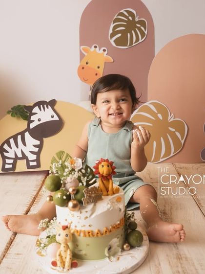 The cake is here. A happy one-year-old sits beside his amazing jungle-themed birthday cake, ready for the cake smash.