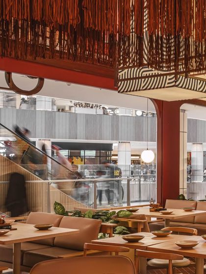 This image captures the bustling ambiance of the mall's escalator in the background, contrasting with the carefully curated and intimate atmosphere inside the restaurant. The design creates a distinct world for diners.