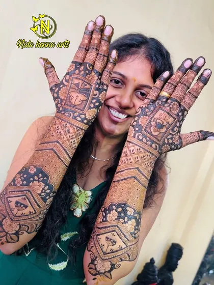 A happy bride showing off her full-coverage mehandi. This design includes geometric patterns, floral bands, and personalized elements.