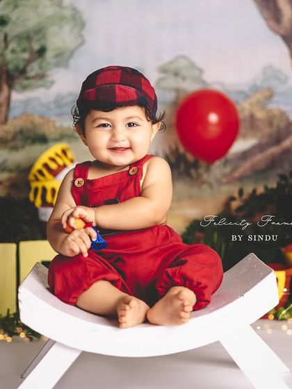 A happy one-year-old boy in his Winnie the Pooh outfit, sitting on a little white bench.