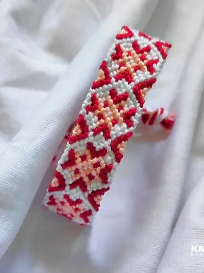 This friendship bracelet features a lovely star or flower-like pattern in shades of red, pink, and white.