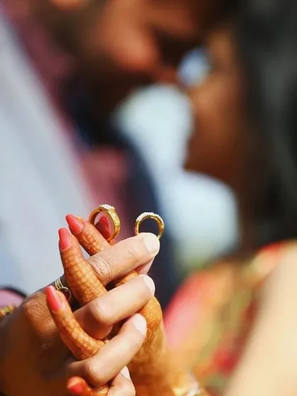 A close-up shot focusing on the couple's hands and their wedding rings, with the couple blurred romantically in the background.