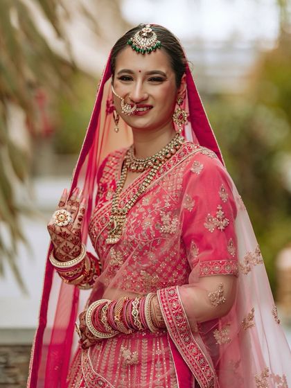 A close-up portrait of the bride in her pink wedding lehenga, showcasing her beautiful smile and traditional jewelry.