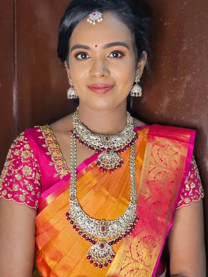 A classic muhurtham look with a vibrant orange and pink saree. The makeup is clean and elegant, letting the bride's natural beauty shine.