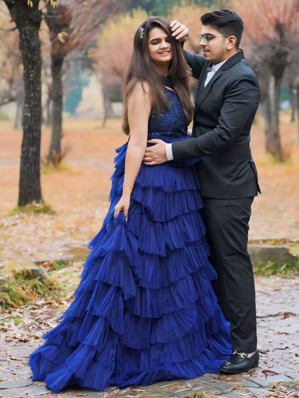 This couple chose a beautiful outdoor setting for their shoot. The bride-to-be's navy blue ruffled gown stands out against the autumn foliage, complemented by her partner's classic black suit.