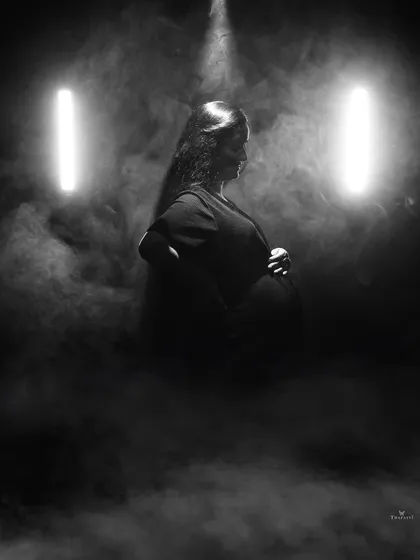 A dramatic profile silhouette enhanced by smoke and two vertical lights. This artistic black and white shot emphasizes the beautiful curve of the baby bump.