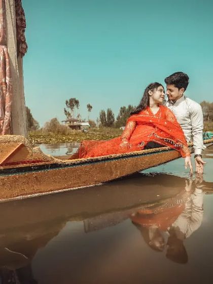 A beautiful shot of a couple in a traditional Shikara boat, their reflection captured in the still water. This is a classic, romantic Kashmir-style photo.