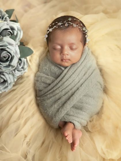 A beautiful, minimalist portrait of a newborn swaddled in a soft grey wrap, complemented by grey roses. The neutral tones create a very serene and modern look.