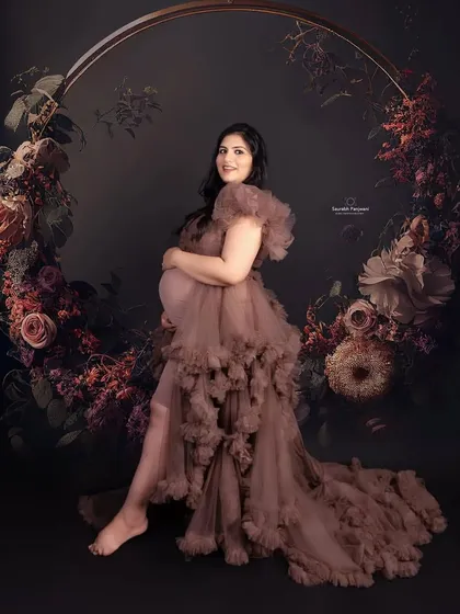A dark and moody studio portrait. This client is wearing a brown ruffled maternity gown, seated in a floral hoop prop that creates a stunning, artistic frame around her.