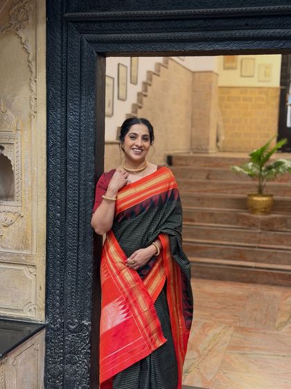 A classic pose showcasing the beautiful black and red saree for a promotional event.