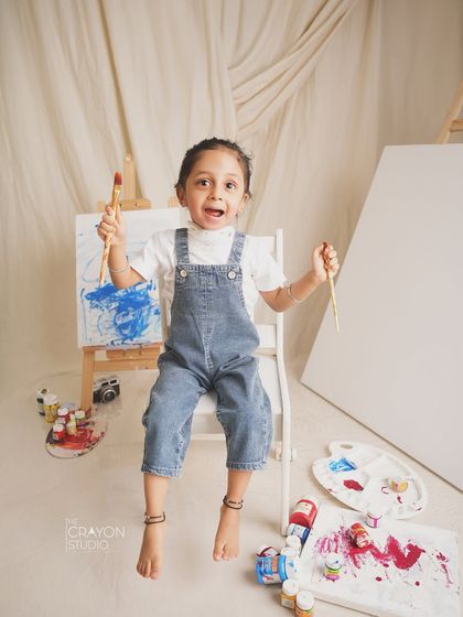 Holding up her paintbrushes with excitement, this little artist is ready to create her masterpiece.
