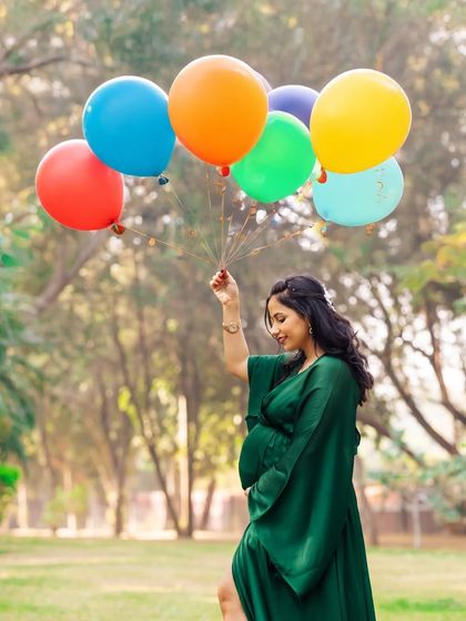 A fun and colorful outdoor shot of a woman in a green gown holding a bunch of bright balloons. This playful image adds a touch of whimsy to the maternity session.