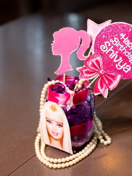 A custom centerpiece for the Barbie party, featuring the iconic silhouette, a personalized "Happy Birthday" sign, and pearl details.