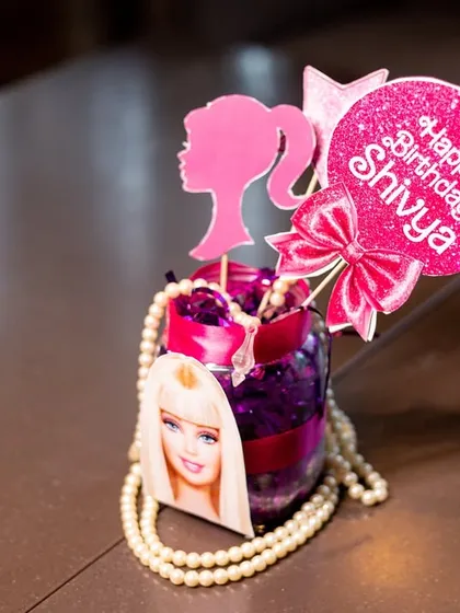 A custom centerpiece for the Barbie party, featuring the iconic silhouette, a personalized "Happy Birthday" sign, and pearl details.