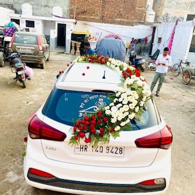 A rear view of a decorated white Hyundai i20. The floral arrangement cascades down one side of the rear windshield, leaving space for visibility.