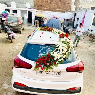 A rear view of a decorated white Hyundai i20. The floral arrangement cascades down one side of the rear windshield, leaving space for visibility.
