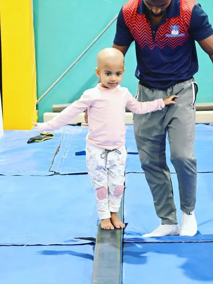 Balance and poise. A coach provides gentle support as a young student gains confidence on the balance beam.