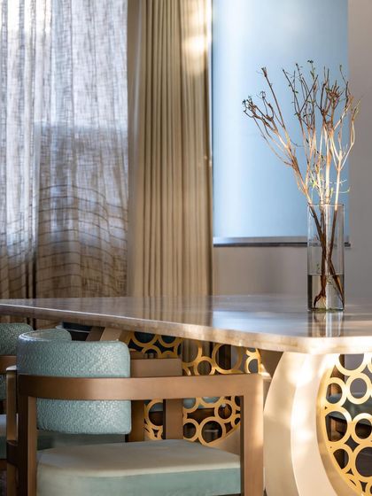 This dining space features a glossy white onyx table as its centerpiece, paired with blue woven leather chairs that add an unexpected pop of color. The open layout and grey floors ground the design, creating a perfect balance of function and flair.