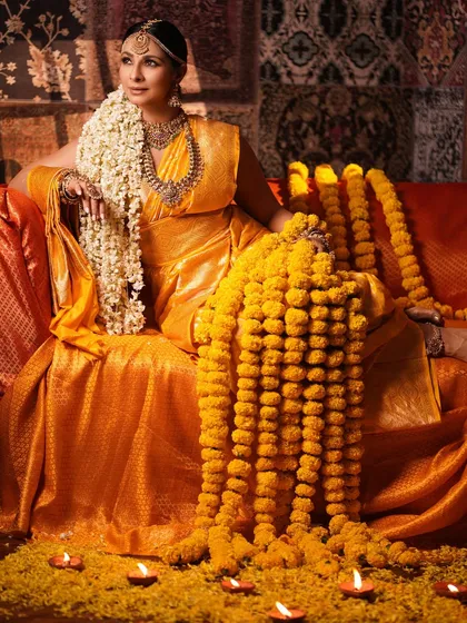 Another perspective of the full setup, showing Tanishaa in a relaxed yet regal pose. The composition with the cascading marigold garlands creates a sense of abundance and festivity.