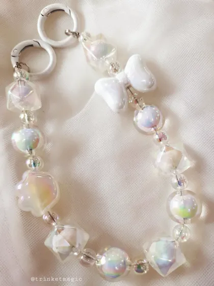 A close-up of the white beaded bag charm, showing the shimmering, multi-faceted beads and the cute bow and paw charms.