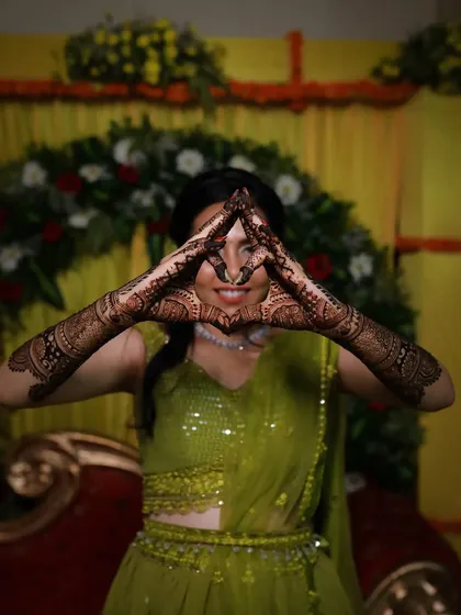 A playful shot from a mehndi ceremony, with the bride making a triangle with her hands to show off the full design.