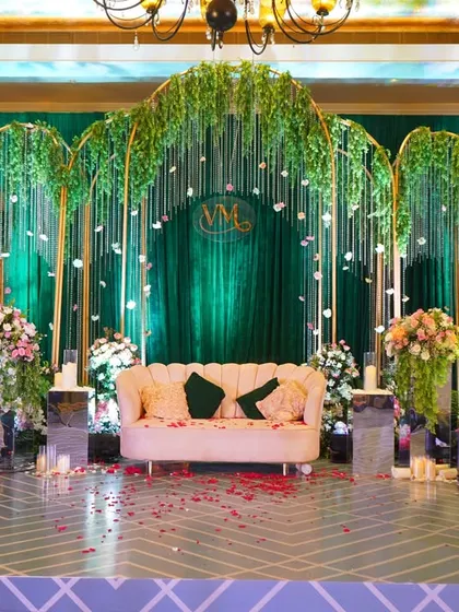 This reception stage is a vision in emerald green. A backdrop of rich velvet is framed by golden arches with cascading greenery and delicate white flowers, creating a look of modern luxury.