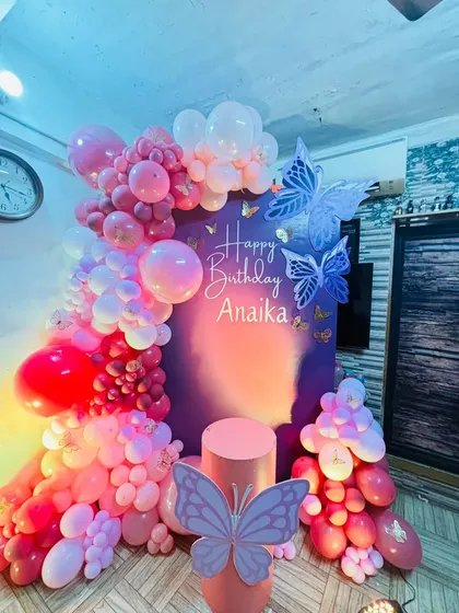 A beautiful butterfly-themed party for Anaika's birthday. The decor features a rich purple and pink balloon arch, accented with large, elegant butterfly cutouts for a touch of whimsy.