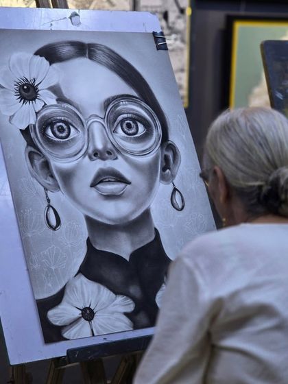From the artist's perspective. This over-the-shoulder view shows the student assessing her work on the easel, a crucial step in the process of creating a balanced charcoal portrait.