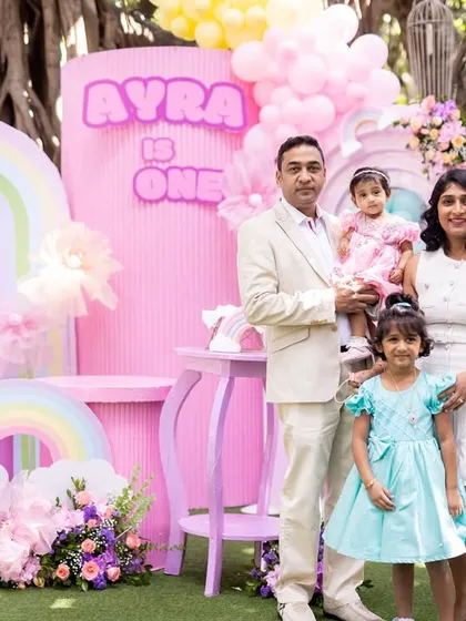 The full family posing in front of the vibrant, pastel-pink backdrop at Ayra's party.