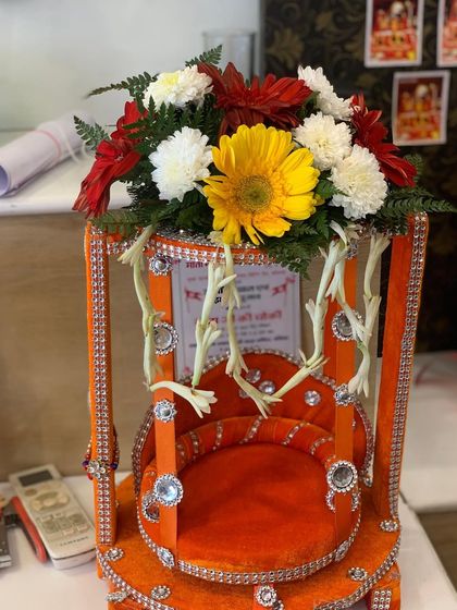 A small, decorated swing ('jhula') for a deity, adorned with a fresh flower arrangement on top. This is perfect for home temples during festivals like Janmashtami.