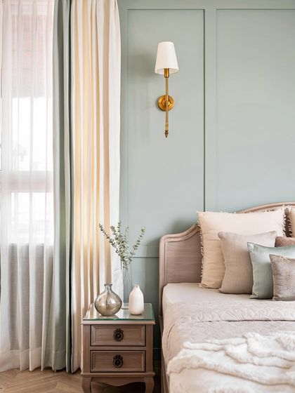 A different angle of the sage green bedroom, showing the layered bedding and the classic wooden nightstand. The color palette is soothing and timeless.