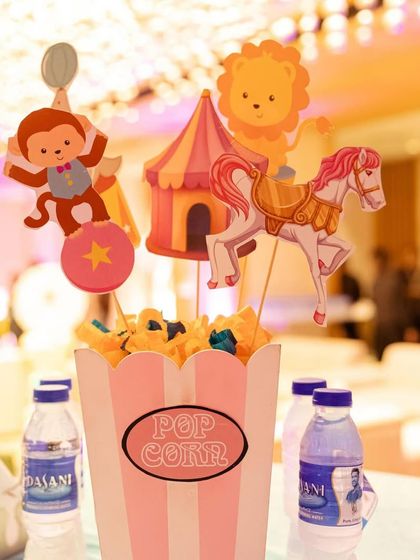 A cute popcorn box centerpiece for a guest table, filled with popcorn and decorated with carnival themed cutouts.